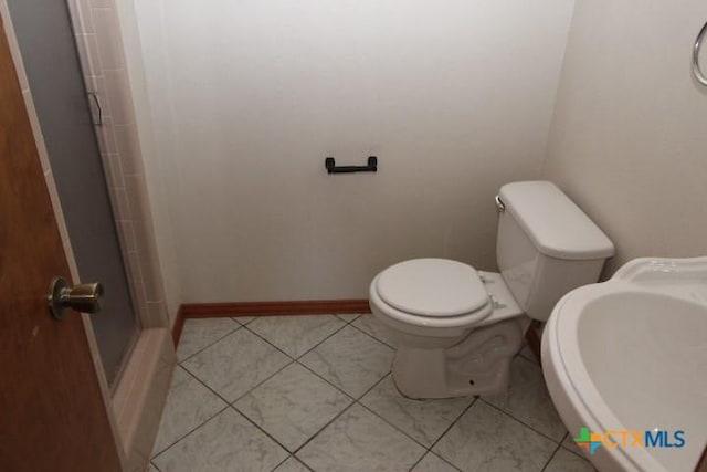 bathroom featuring tile patterned flooring, a shower stall, baseboards, toilet, and a sink