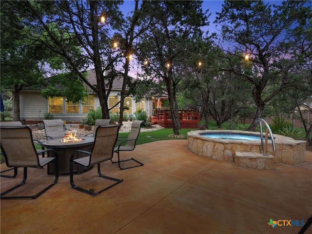 patio terrace at dusk with an in ground hot tub, a wooden deck, and a fire pit