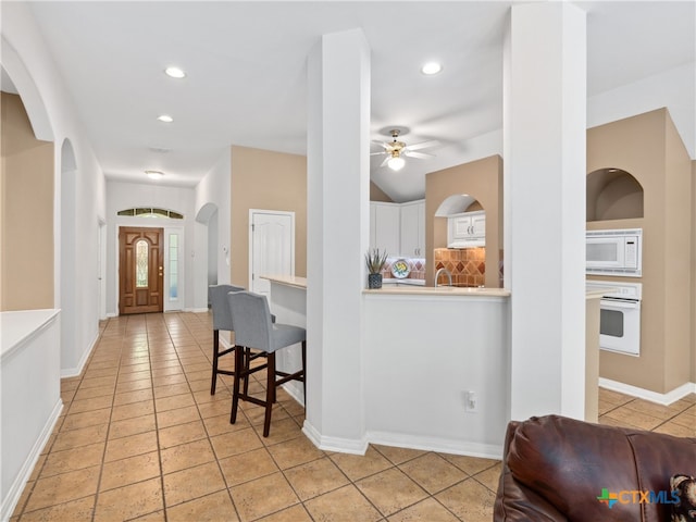 kitchen with lofted ceiling, backsplash, white cabinets, light tile patterned floors, and white appliances