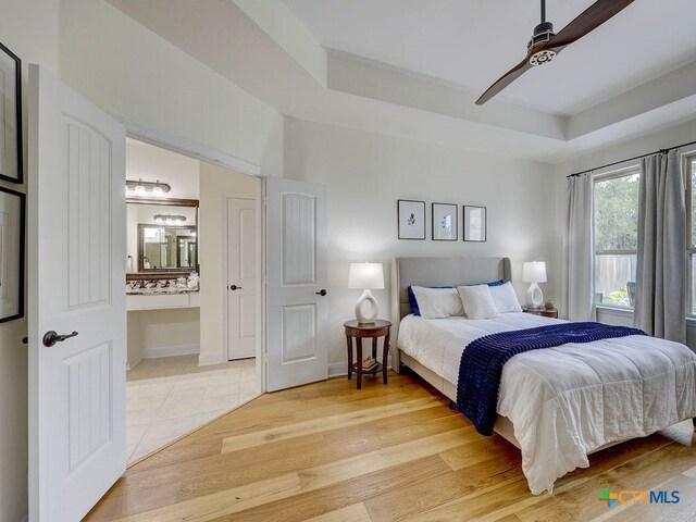 599 Mission Hill Run, New Braunfels, TX 78132 - bedroom with a tray ceiling, ensuite bath, ceiling fan, and light wood-style flooring