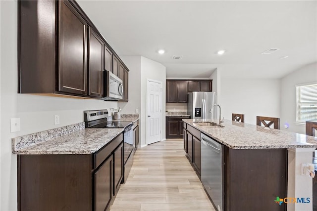 8903 Cantera Ridge Rd, Temple, TX 76502 - kitchen featuring stainless steel appliances, dark brown cabinets, a kitchen island with sink, light wood-style floors, and light stone countertops