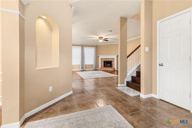 tiled entrance foyer featuring a fireplace, ceiling fan, and crown molding