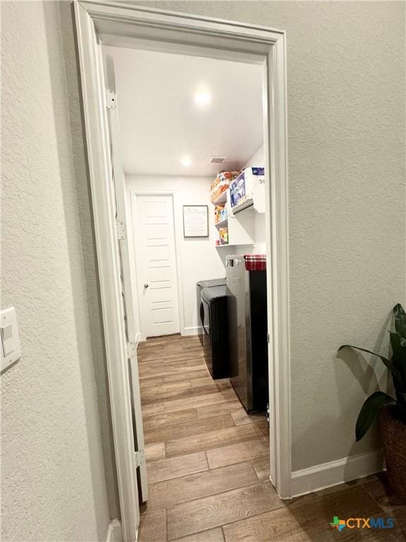 washroom with laundry area, baseboards, a textured wall, wood finished floors, and washing machine and clothes dryer