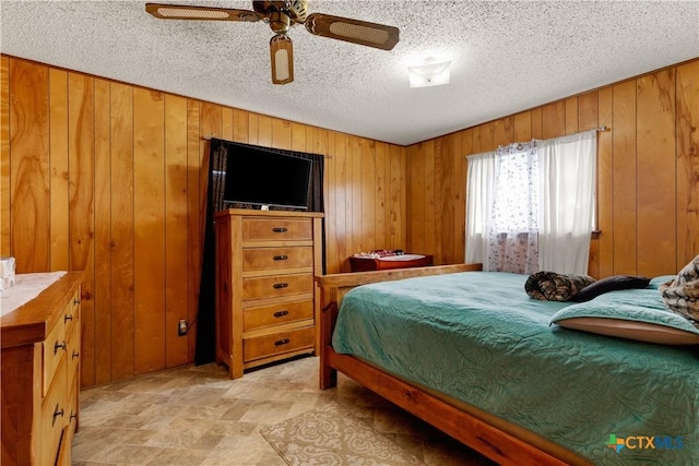 bedroom with ceiling fan, a textured ceiling, and wooden walls