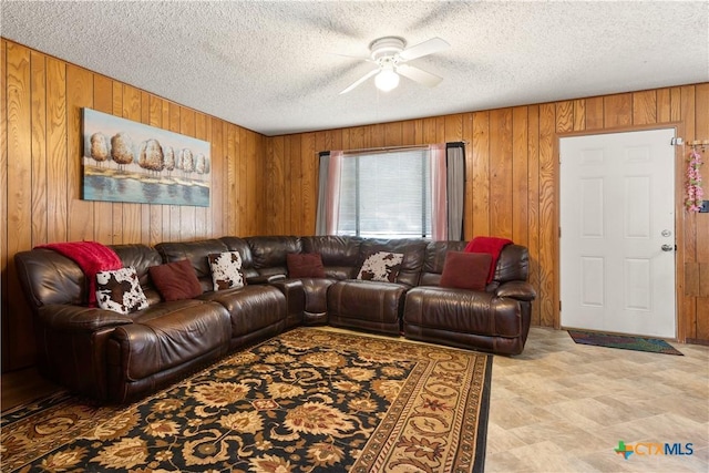 living room with a textured ceiling, ceiling fan, and wooden walls