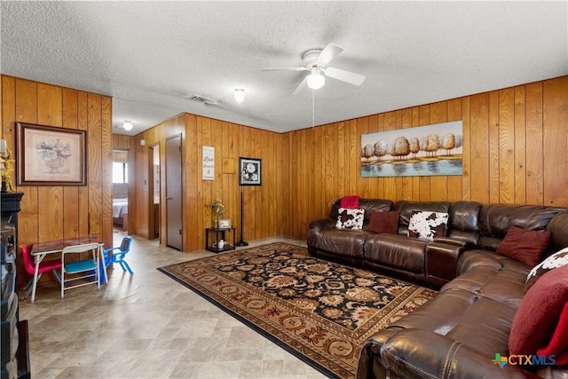 living room with wooden walls, ceiling fan, and a textured ceiling