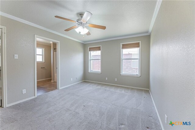 carpeted spare room with crown molding, baseboards, and a ceiling fan