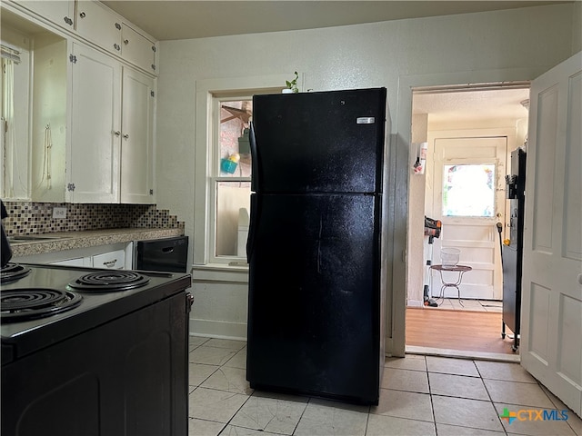 kitchen featuring light tile patterned flooring, tasteful backsplash, range with electric cooktop, white cabinets, and black refrigerator