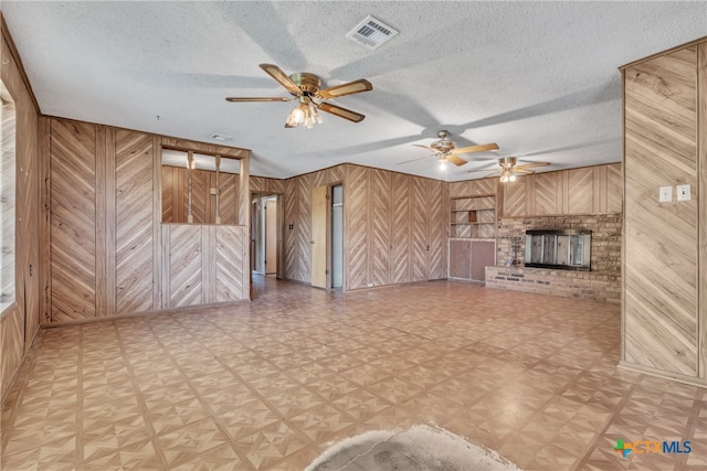 unfurnished living room featuring a fireplace, wood walls, and a textured ceiling