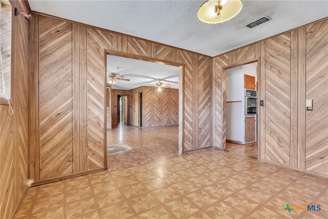 spare room with ceiling fan, a textured ceiling, wooden walls, and light parquet flooring