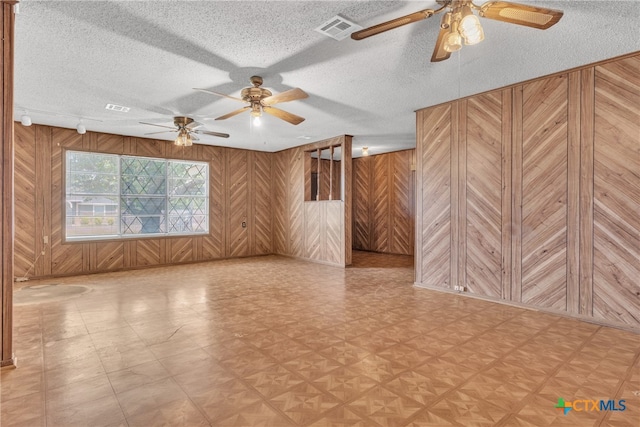 spare room featuring wooden walls, a textured ceiling, and ceiling fan