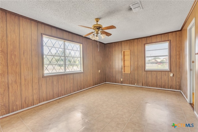 unfurnished room with wood walls, a wealth of natural light, and ceiling fan