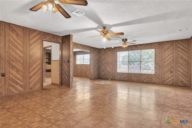 empty room with wood walls, a textured ceiling, and ceiling fan