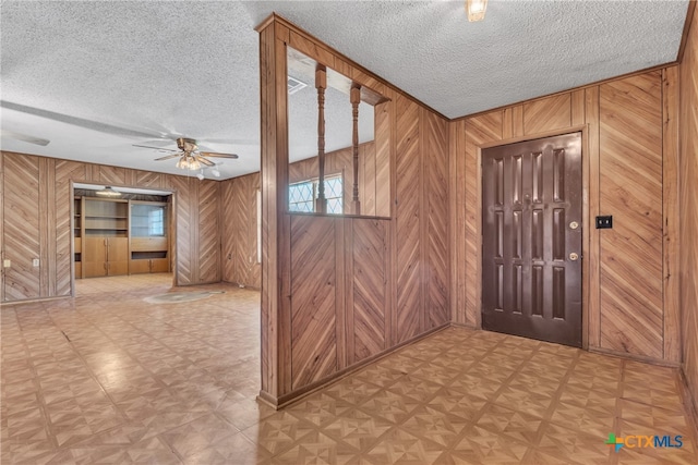 foyer with wood walls, ceiling fan, and a textured ceiling