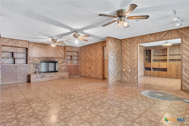 unfurnished living room featuring built in features, a fireplace, a textured ceiling, wooden walls, and ceiling fan