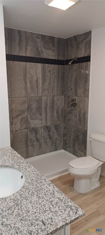 bathroom featuring wood-type flooring, vanity, toilet, and a tile shower