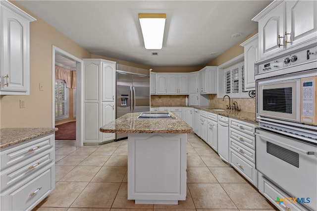 kitchen featuring light stone counters, stainless steel appliances, sink, a center island, and white cabinetry