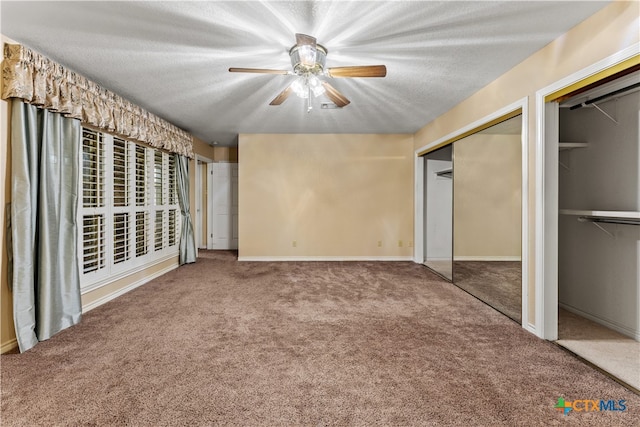 unfurnished bedroom with a textured ceiling, ceiling fan, carpet, and two closets