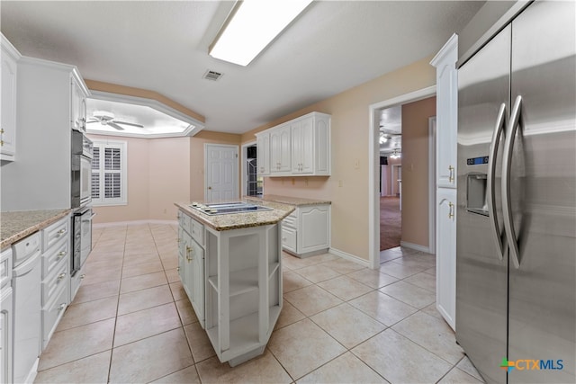 kitchen with light stone countertops, a kitchen island, stainless steel fridge with ice dispenser, stovetop, and white cabinets