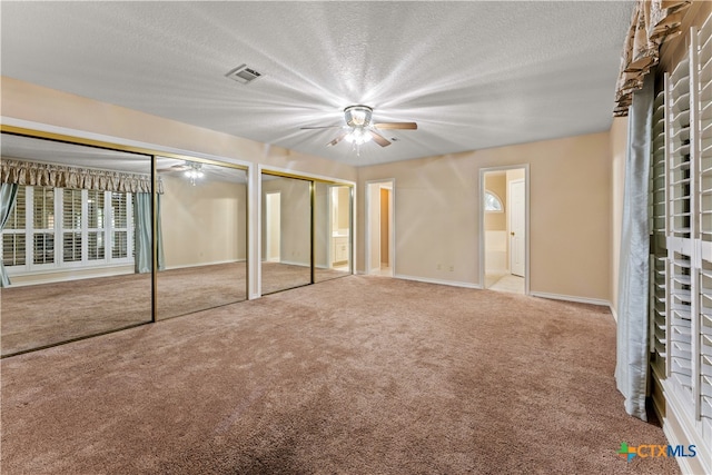 unfurnished bedroom featuring carpet flooring, two closets, ceiling fan, and a textured ceiling