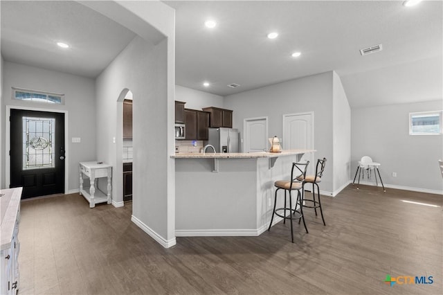 kitchen featuring visible vents, a breakfast bar area, dark wood finished floors, arched walkways, and appliances with stainless steel finishes