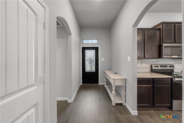 mudroom with dark wood-type flooring, arched walkways, and baseboards