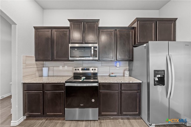 kitchen with light stone countertops, dark brown cabinetry, stainless steel appliances, light wood finished floors, and backsplash