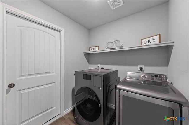 clothes washing area featuring baseboards, washing machine and dryer, visible vents, laundry area, and wood finished floors