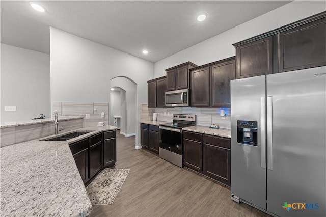 kitchen with a sink, dark brown cabinets, wood finished floors, stainless steel appliances, and backsplash