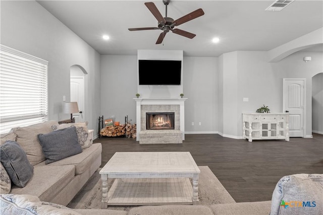 living area featuring visible vents, arched walkways, ceiling fan, dark wood-type flooring, and a glass covered fireplace