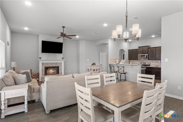 dining room with arched walkways, a tile fireplace, dark wood-style floors, and ceiling fan with notable chandelier