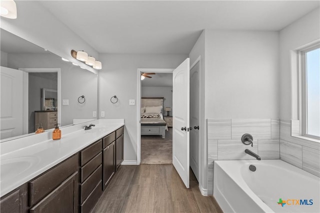 full bathroom with a garden tub, ensuite bath, a ceiling fan, wood finished floors, and double vanity