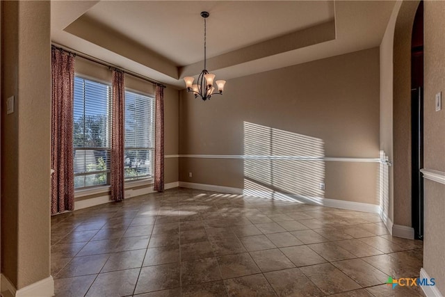 tiled spare room featuring a tray ceiling, plenty of natural light, and an inviting chandelier