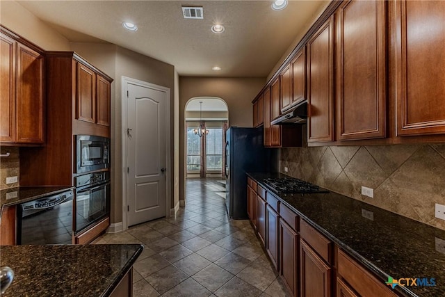 kitchen with backsplash, dark stone counters, an inviting chandelier, black appliances, and dark tile patterned floors