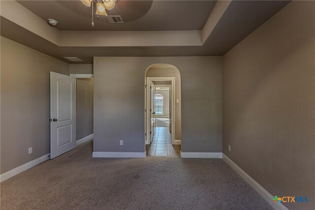 unfurnished room featuring a raised ceiling, light carpet, and ceiling fan