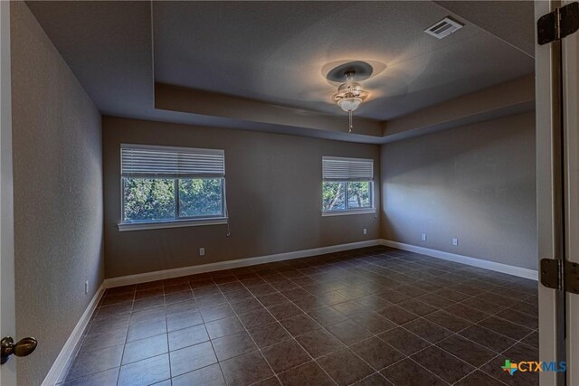 tiled spare room featuring a raised ceiling and ceiling fan