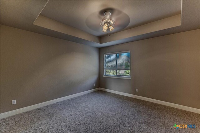 carpeted empty room with a raised ceiling and ceiling fan