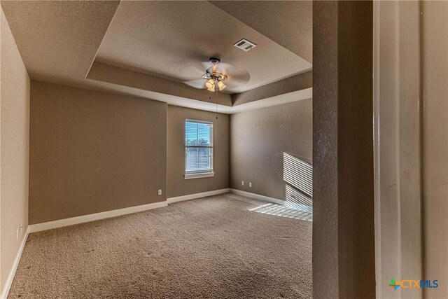 empty room featuring a raised ceiling, ceiling fan, carpet floors, and a textured ceiling