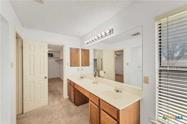 bathroom with a sink, visible vents, a textured ceiling, and double vanity