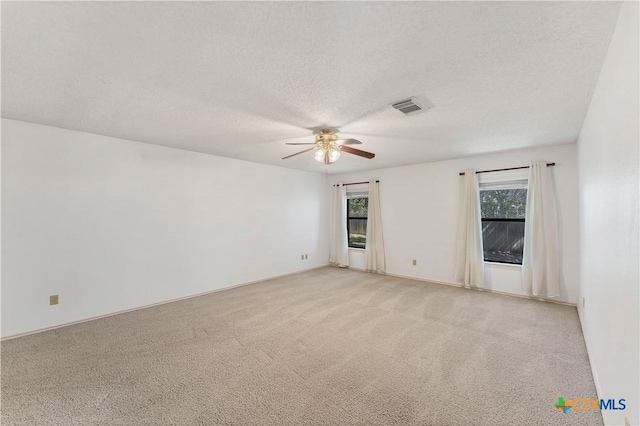 empty room with visible vents, light colored carpet, a textured ceiling, and a ceiling fan