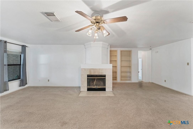 unfurnished living room featuring visible vents, built in shelves, carpet, ceiling fan, and a fireplace