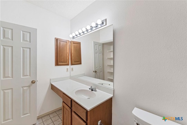 half bathroom with a textured ceiling, toilet, vanity, and tile patterned flooring