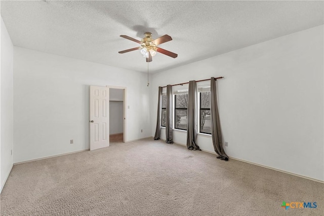 unfurnished bedroom featuring a textured ceiling, a walk in closet, a ceiling fan, and light carpet