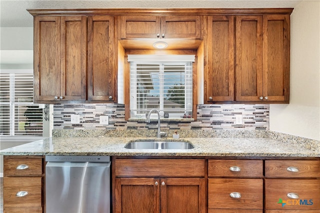 kitchen featuring stainless steel dishwasher, sink, backsplash, and light stone countertops