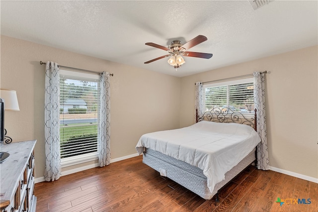 bedroom featuring ceiling fan, multiple windows, and dark hardwood / wood-style flooring