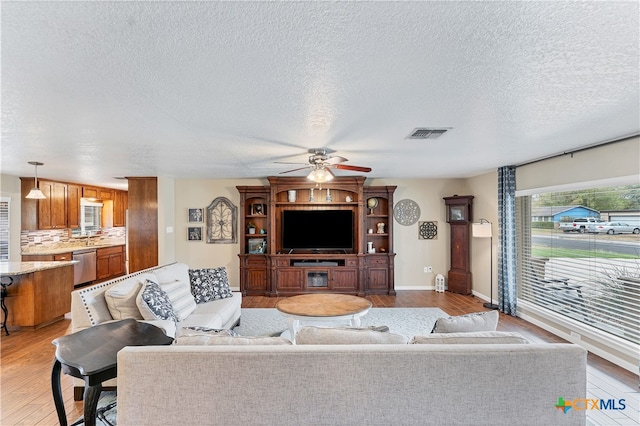 living room with light wood-type flooring, a textured ceiling, and ceiling fan