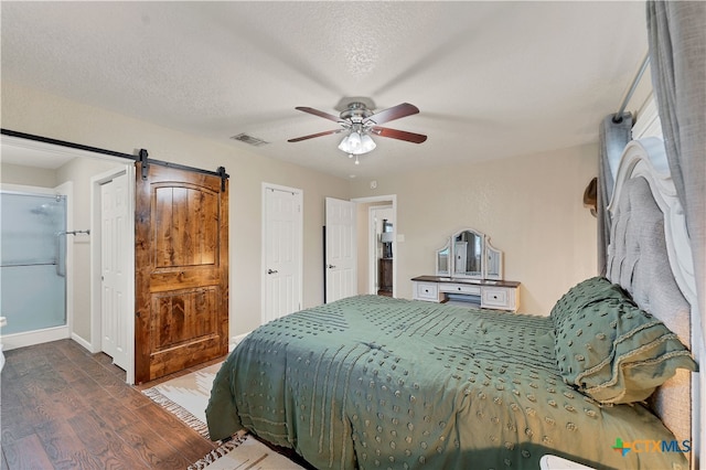 bedroom featuring a textured ceiling, a barn door, ceiling fan, and dark hardwood / wood-style floors