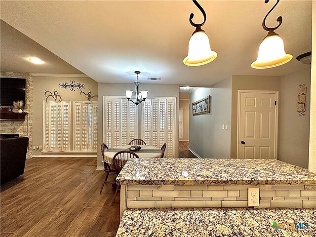 kitchen with light stone counters, ornamental molding, a chandelier, dark wood-type flooring, and pendant lighting