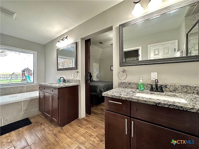 bathroom with vanity, hardwood / wood-style flooring, and a relaxing tiled tub