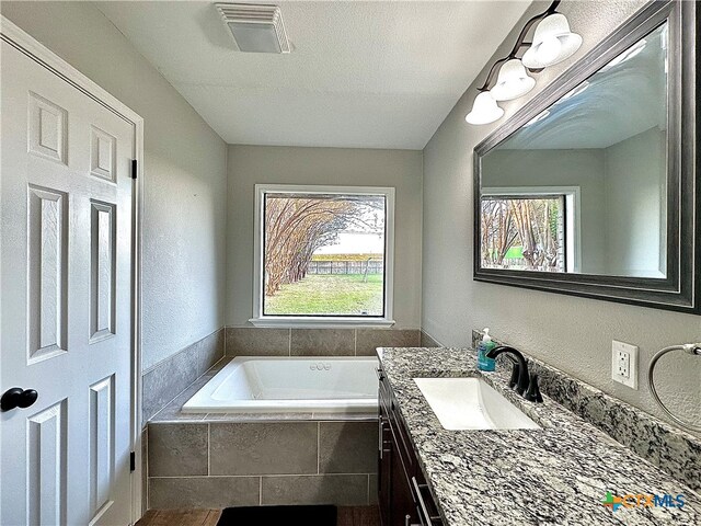 bathroom with vanity, tiled tub, a textured ceiling, and plenty of natural light